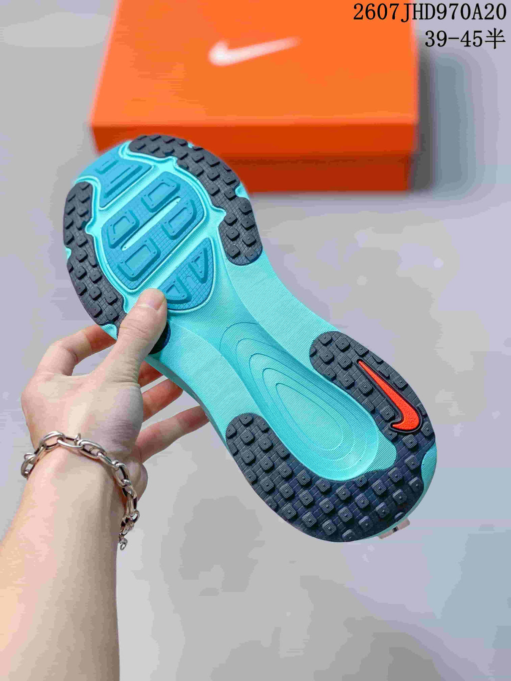 Bottom view of a turquoise and black textured outsole with an orange accent, with an orange Nike shoebox in the background.