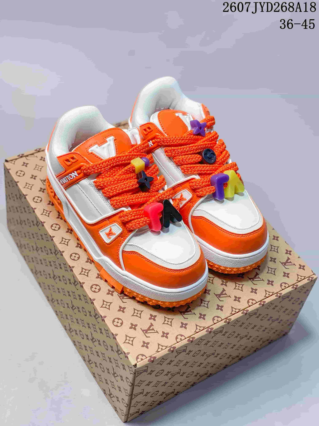 Pair of white and orange low-top sneakers displayed on a patterned box, with orange laces and decorative lace accessories.