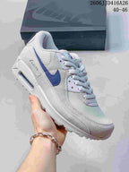 Angled side view of the white and blue Nike Air Max 90 sneaker showing the layered upper and heel detail.