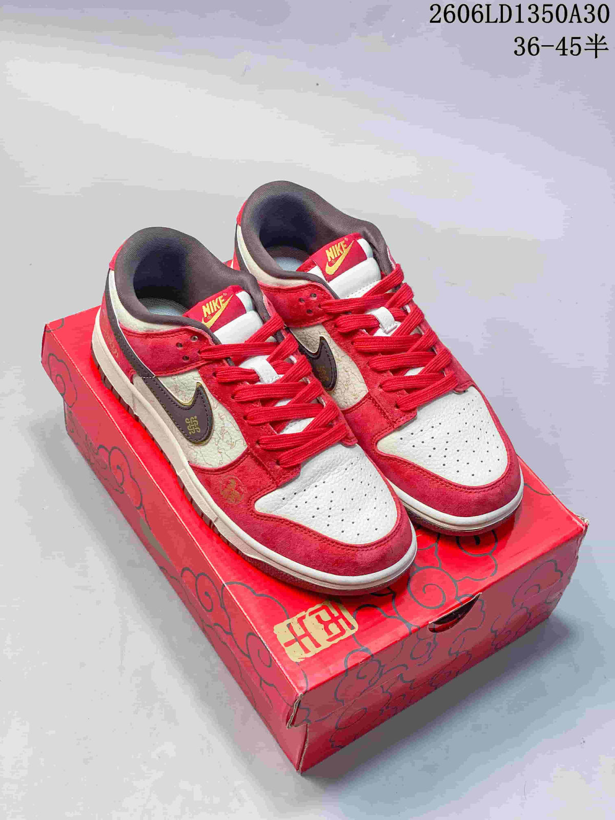 Pair of red, cream, and dark brown Nike SB Dunk Low sneakers on a patterned red box