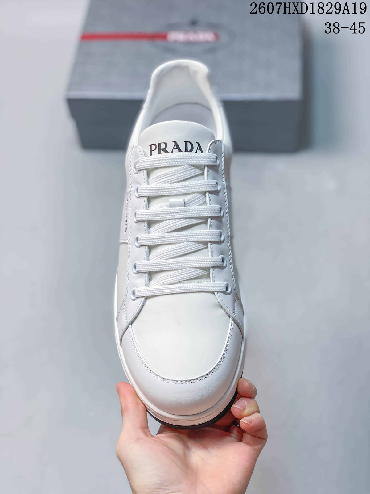 Top view of the white sneaker showing the rounded toe, white laces and Prada-branded tongue.