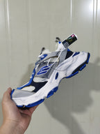 Angled view of the white, grey, and blue sneaker showing its layered upper, side logo, laces, and blue outsole accents.