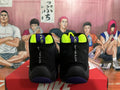 Rear view of black Nike high-top basketball sneakers with neon yellow lining, purple outsole accents, and “THE GLOVE” lettering, displayed on a Nike box.