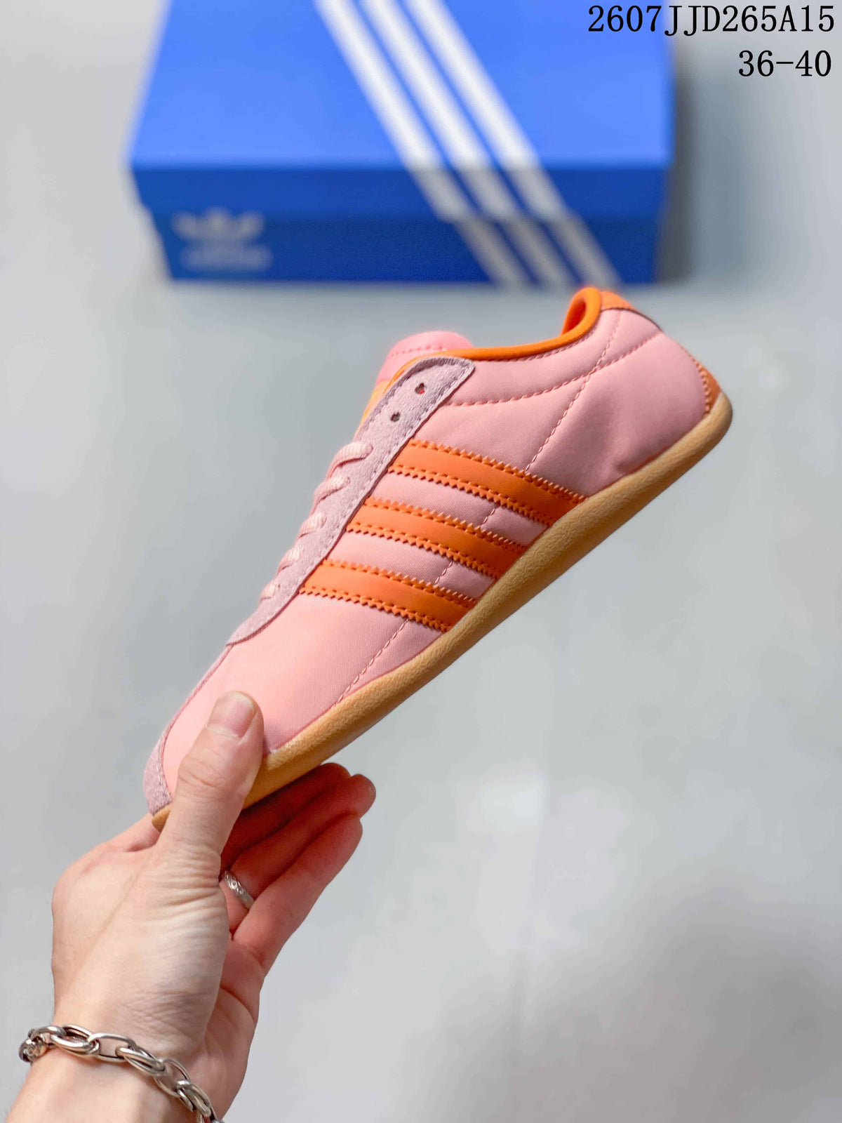 Side profile showing the pink upper, three orange stripes, lace panel, and gum-colored sole.