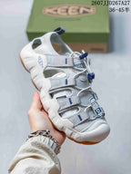 Angled side view of the white and gray KEEN sandal showing the closed toe, open side panels, heel pull tab, and textured gum-colored outsole.