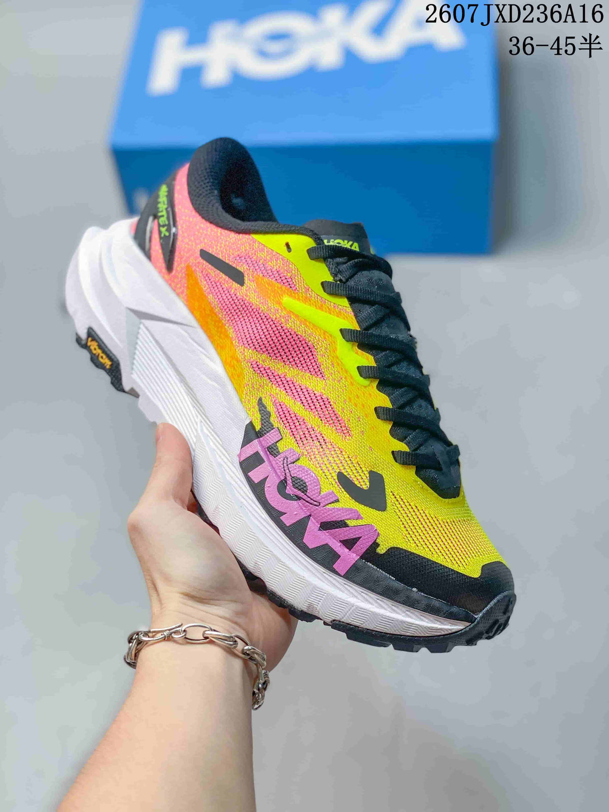 Side view of a yellow and pink Hoka MAFATE X shoe with black laces, a raised white midsole, and dark outsole.
