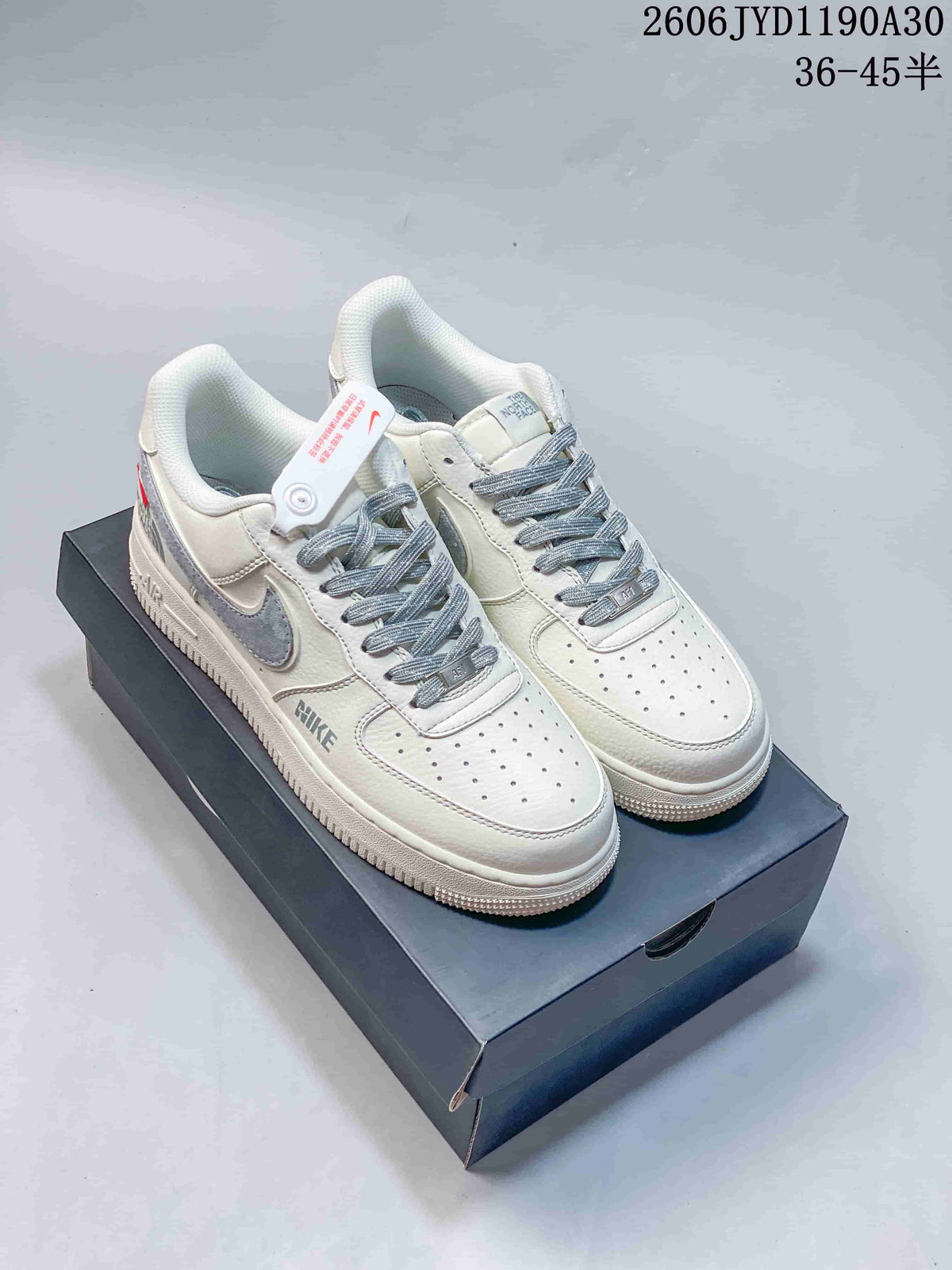 Cream low-top sneakers with gray accents and patterned laces, shown on a dark box.