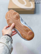 Underside of a silver sneaker showing the gum-colored outsole and circular traction patterns.