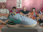 Side view of a light blue Nike basketball shoe with a teal side logo and dark olive heel panel