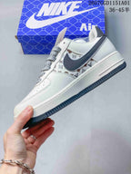Side profile of a white sneaker with a dark gray Swoosh, monogram-style print, and patterned laces.