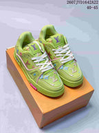 Pair of green Louis Vuitton Trainer low-top sneakers displayed on an orange shoe box, with white laces, multicolor motifs, and pink accents.