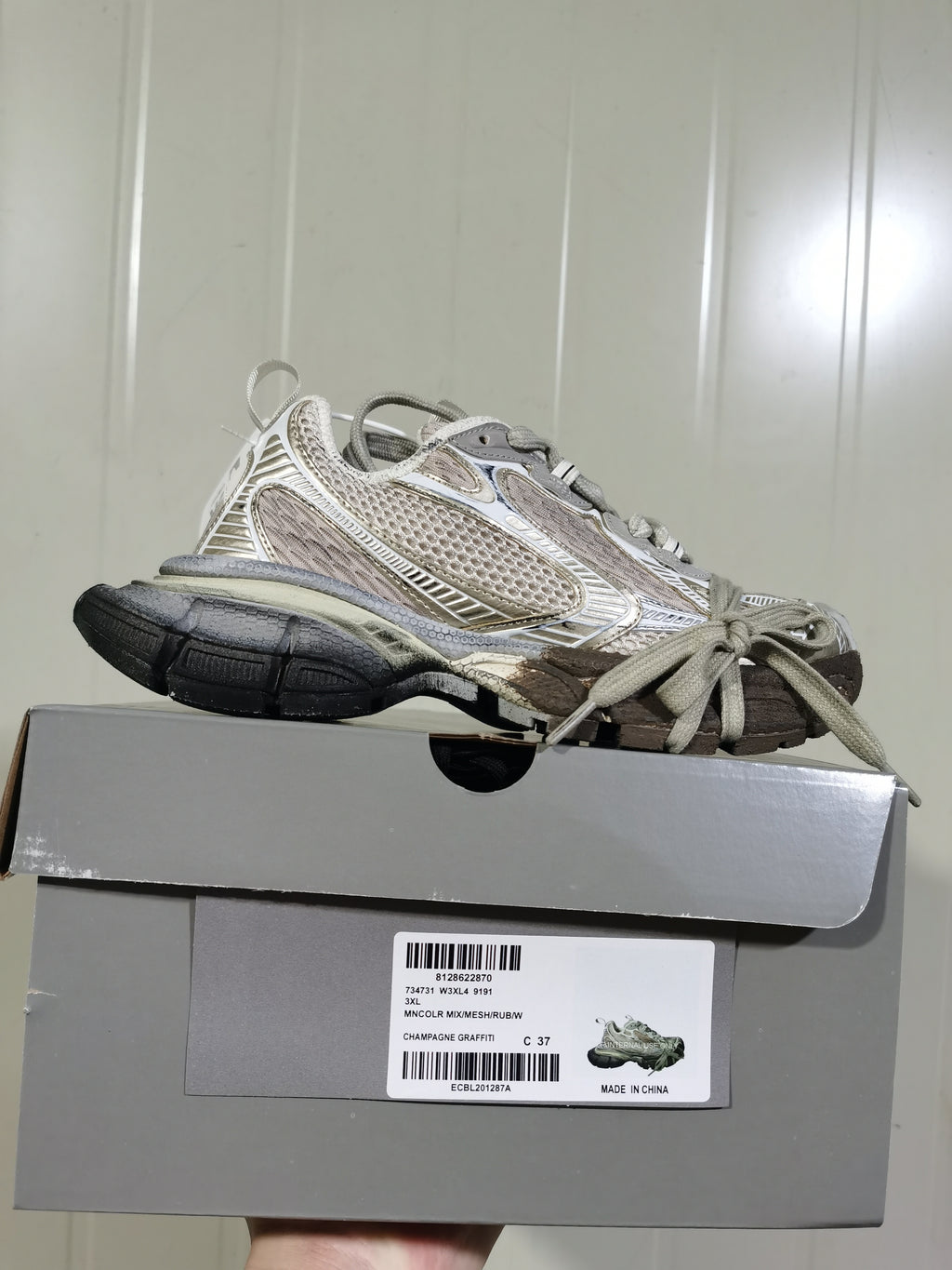 Side view of the sneaker resting on its box; the label shows 3XL, style code 9191, and champagne graffiti color text.