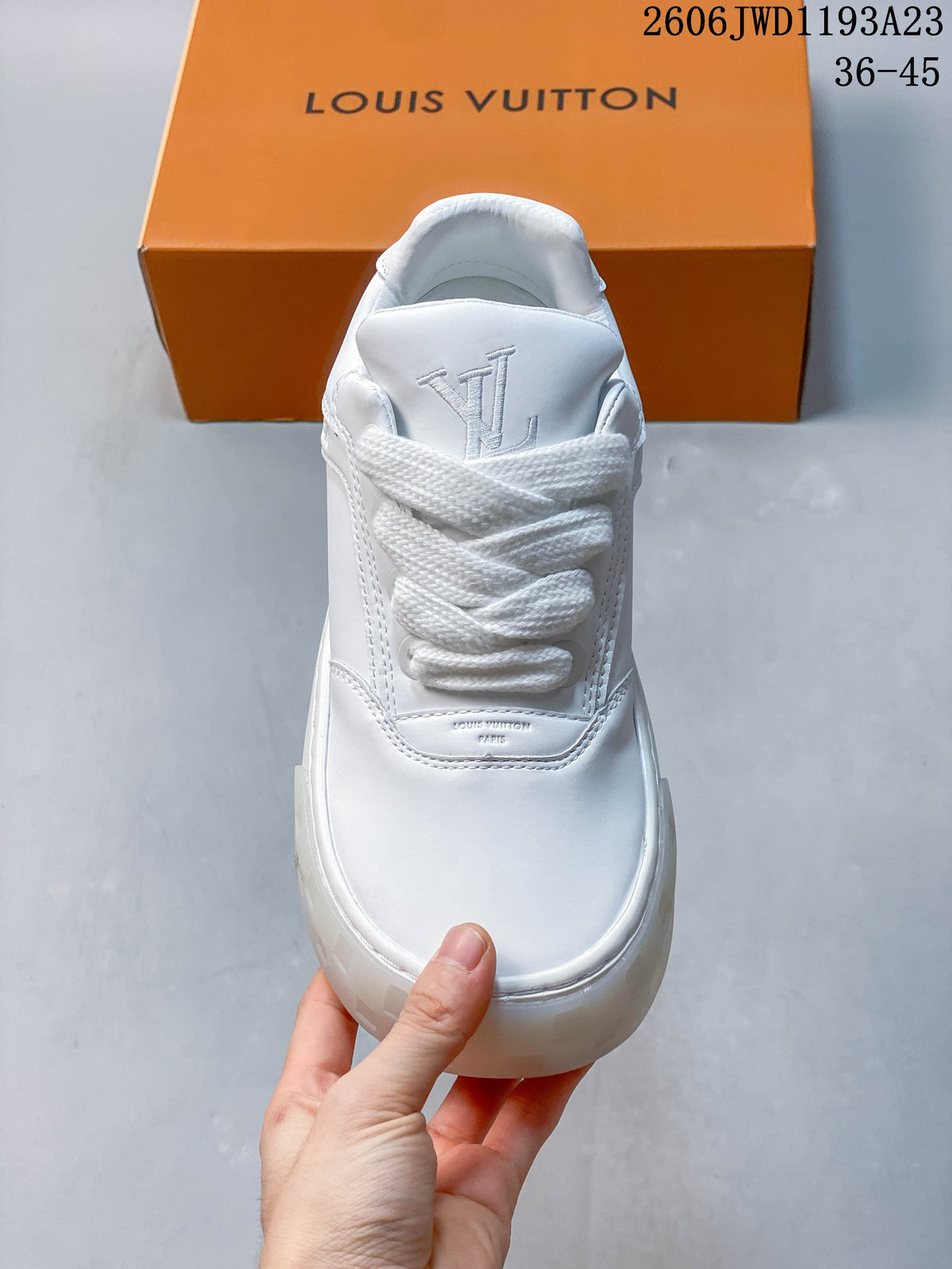 Front view of a white sneaker with wide laces and a monogrammed tongue