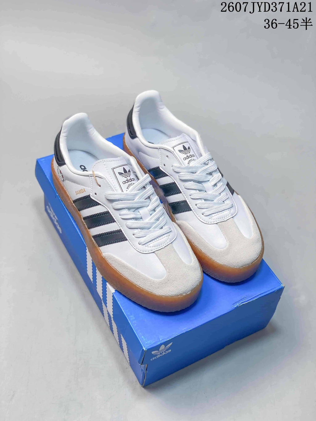 Pair of white and black adidas Sambae sneakers with gum soles displayed on a blue shoebox.