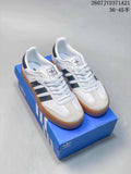 Pair of white and black adidas Sambae sneakers with gum soles displayed on a blue shoebox.