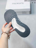 Underside view of a trainer showing the dark patterned rubber outsole and light-colored central section.