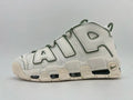 Side view of a white Nike Air More Uptempo sneaker with dark green accents, oversized AIR lettering, and a chunky segmented sole.
