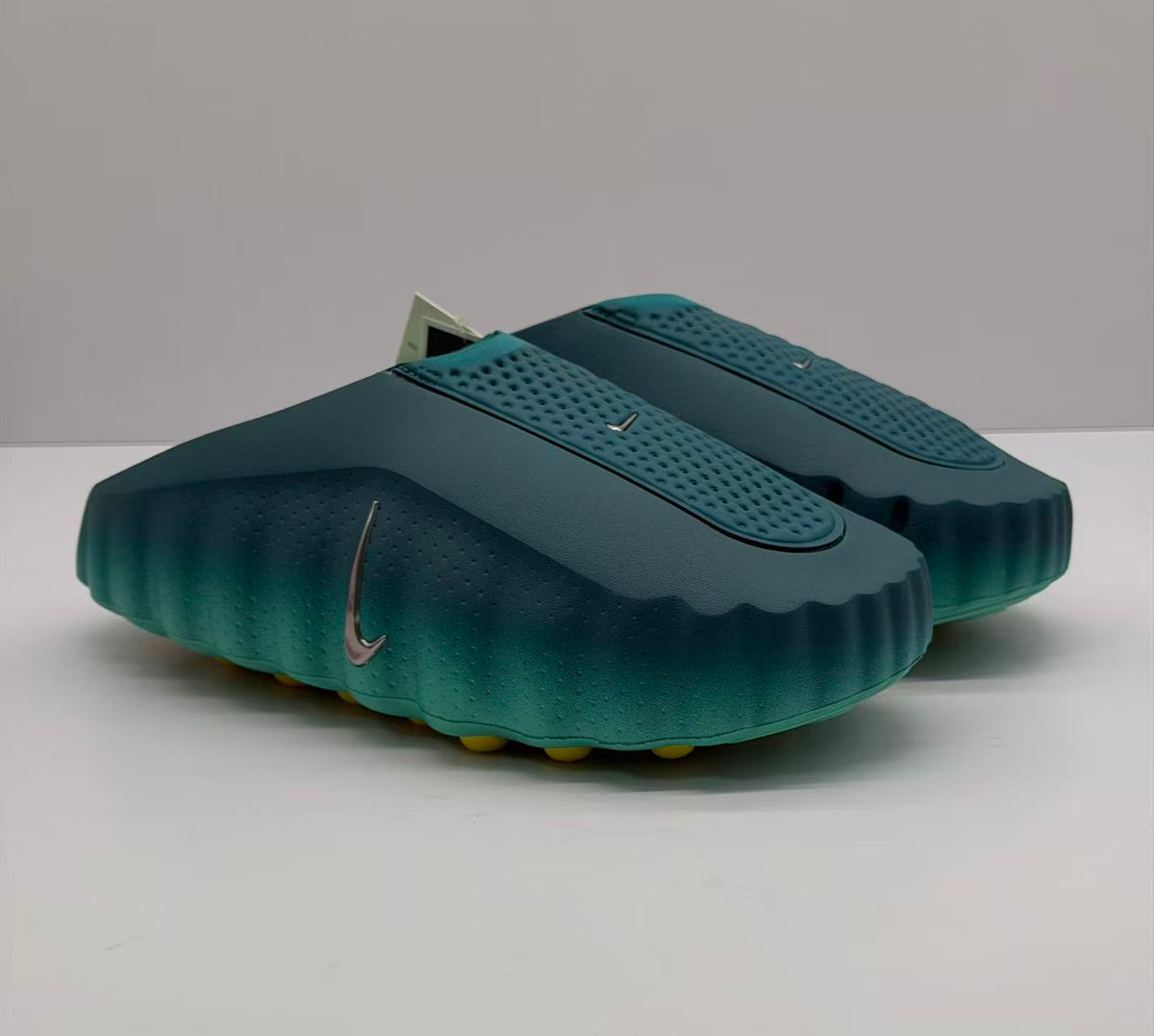 Angled view of the pair of green slides with perforated upper panels and Nike branding.