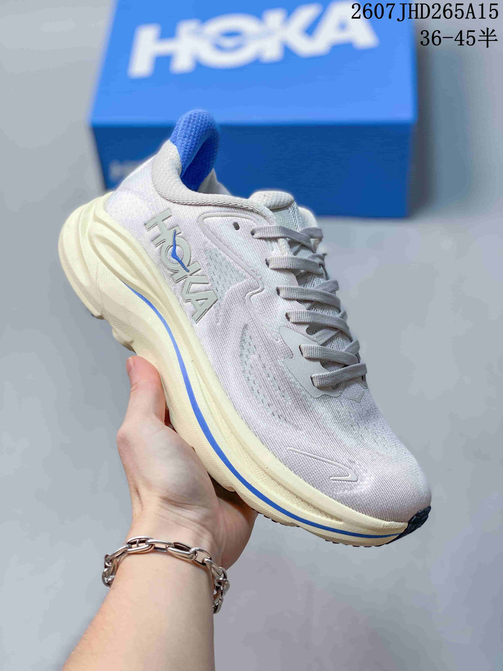 Angled side view of a light-colored HOKA Clifton 10 sneaker showing the logo, blue accent stripe, and cushioned sole.