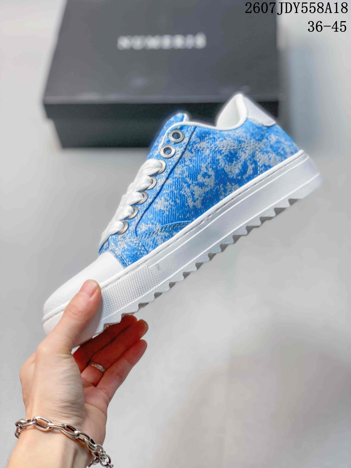 Side view of the blue low-top sneaker showing the patterned upper, white laces, metal eyelets, and raised textured sole.