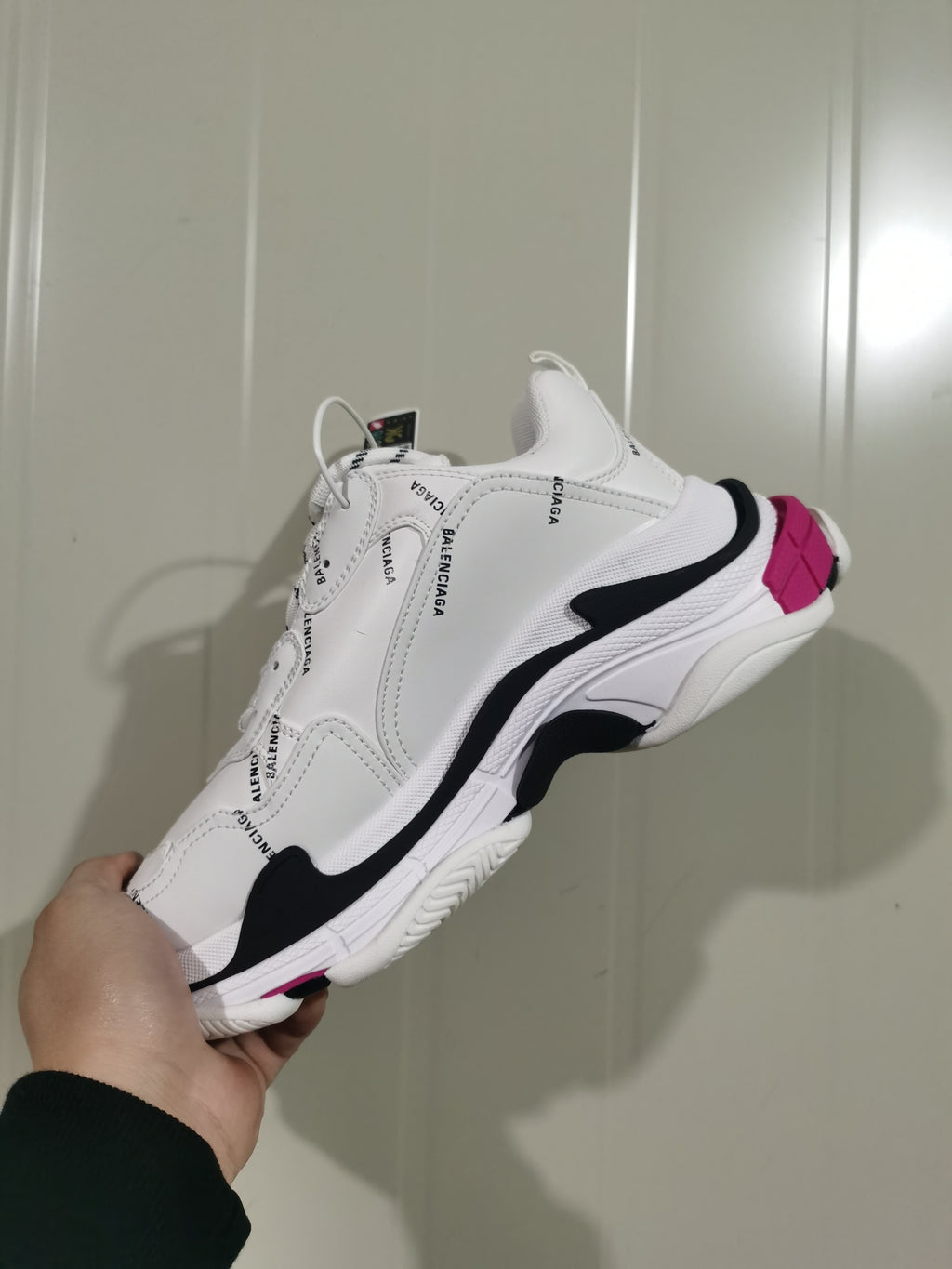 Side and outsole view of a white Balenciaga Triple S sneaker with black overlays and pink heel accents.