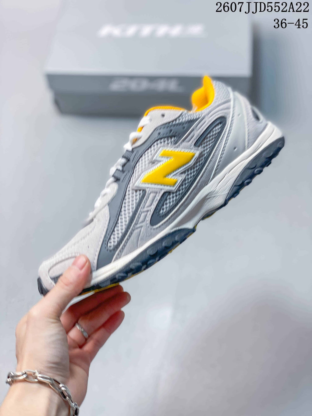 Side profile highlighting the grey layered upper, yellow New Balance logo, and dark outsole.