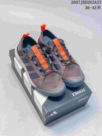 Pair of brown and dark gray Adidas Terrex sneakers with bright orange lace straps and contrasting toe bumpers.