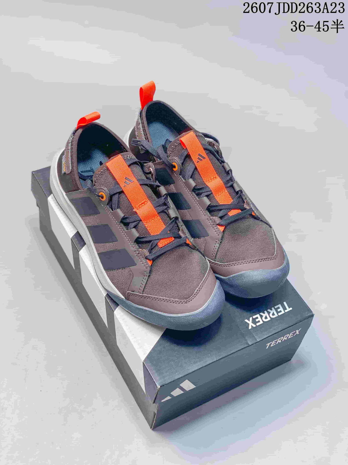Pair of brown and dark gray Adidas Terrex sneakers with bright orange lace straps and contrasting toe bumpers.
