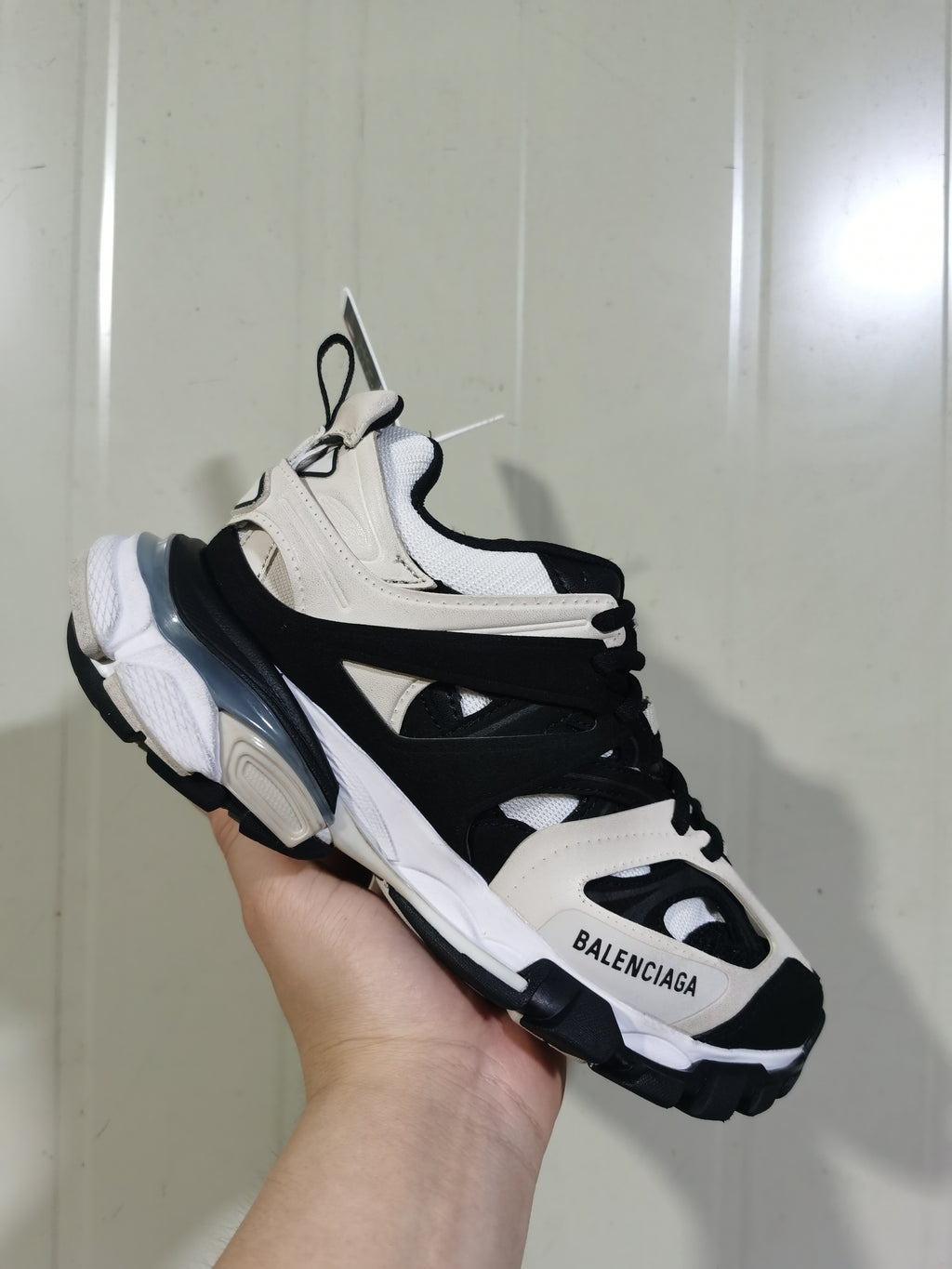 Handheld view of Balenciaga Track sneakers in grey, black, and white with layered panels and a chunky sole.