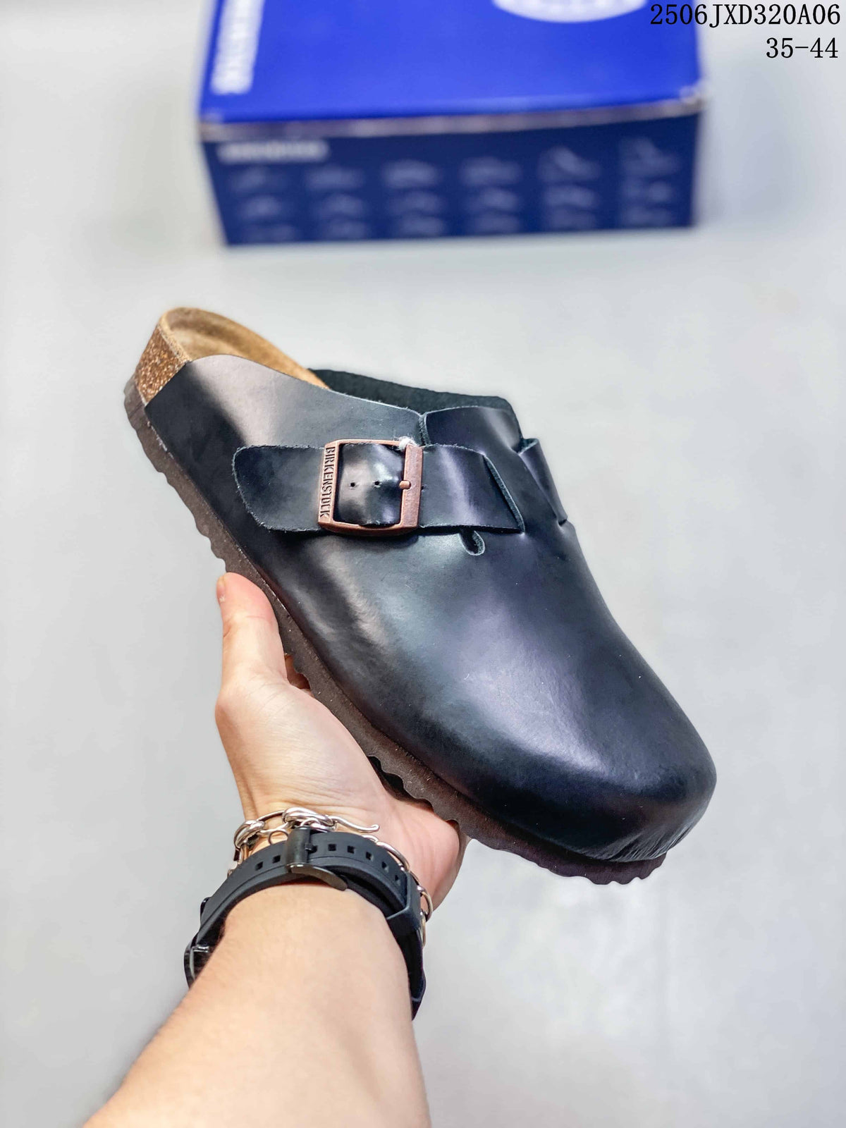 Angled close-up of a black buckle clog showing the smooth upper, metal buckle, footbed, and textured outsole.