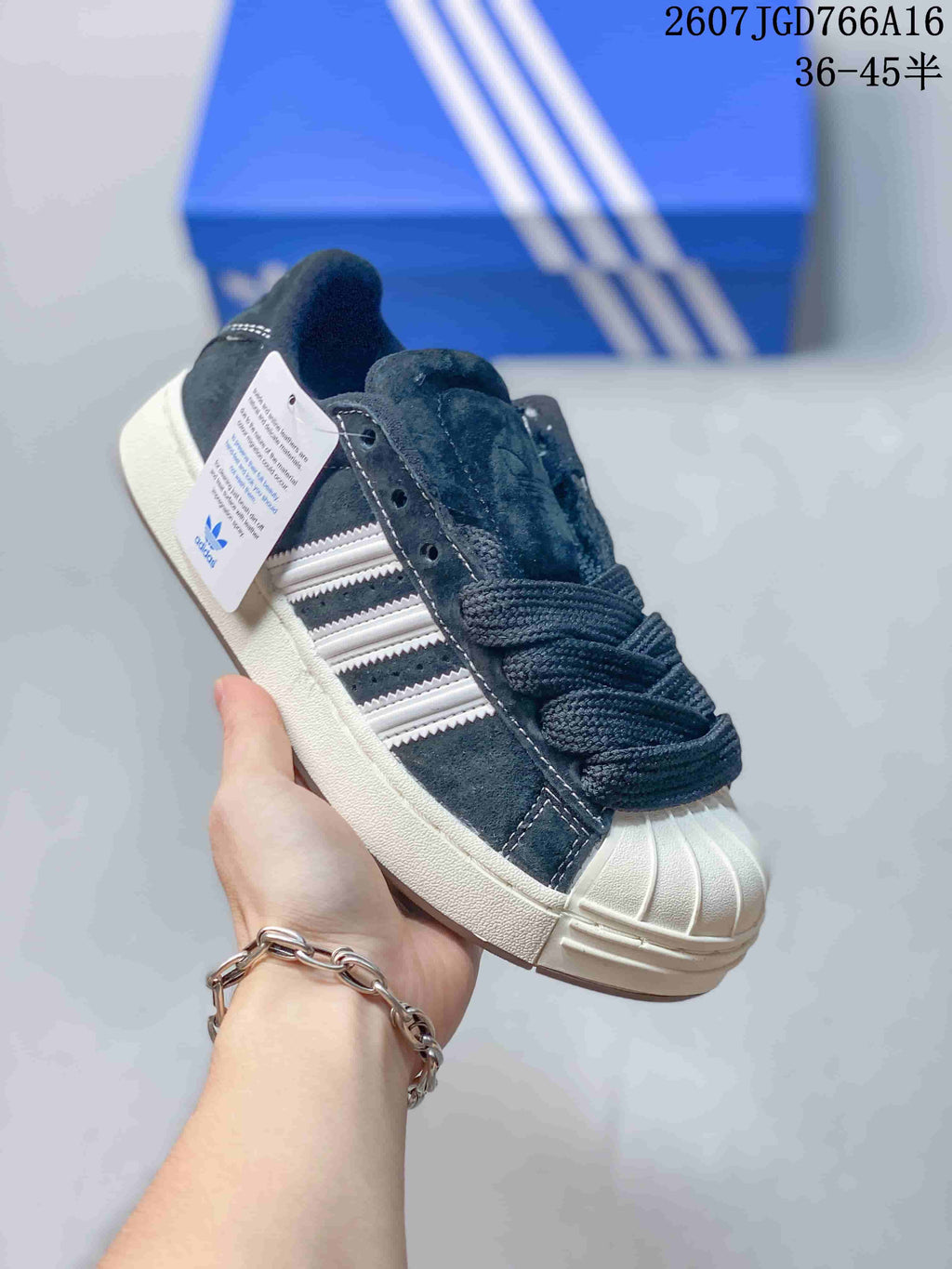 Close-up side view of a black and gray adidas shell-toe sneaker showing the three stripes, laces, stitching, and cream-colored sole.