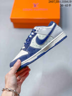 Side profile of a white and navy low-top sneaker showing layered panels, contrast stitching, patterned side material, and a navy outsole.