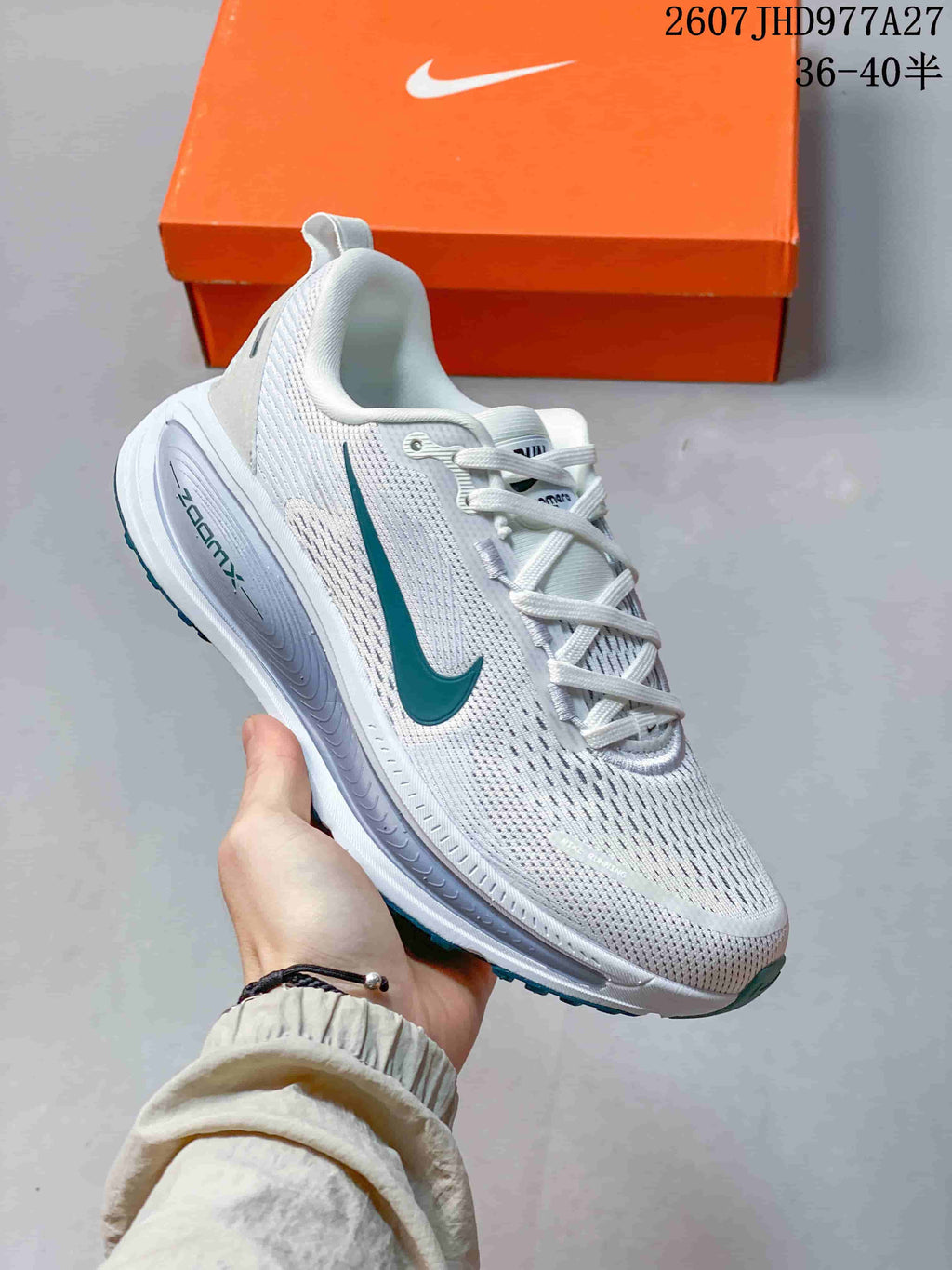 Angled side view of the white sneaker showing the teal Swoosh, mesh-textured upper, layered sole and teal outsole accents; overlay text shows style code 2607JHD977A27 and sizes 36–40.5.