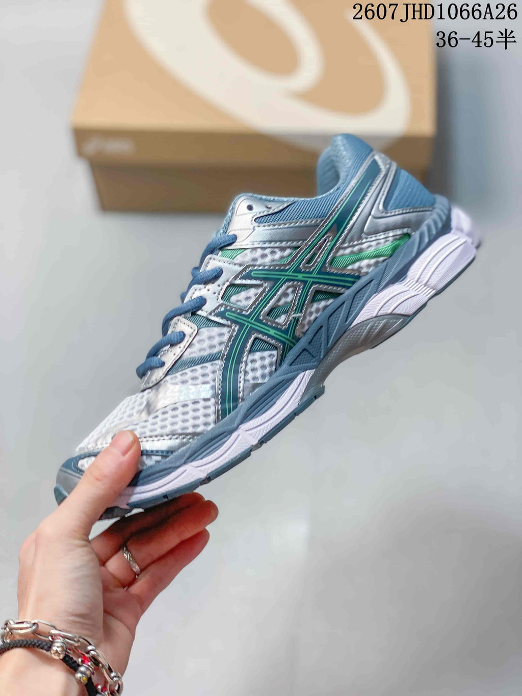 Side view of the ASICS Gel-Cumulus 16 sneaker showing layered mesh panels, blue overlays, silver details and green branding accents.