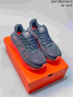 Pair of dark Nike Air Pegasus Premium sneakers with bright red sole units displayed on an orange shoebox.