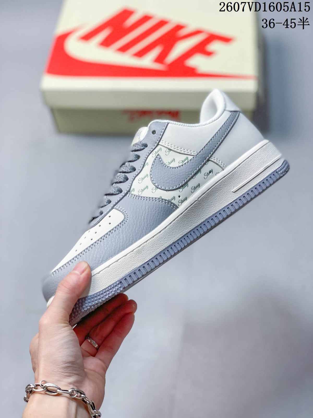 Side profile showing the grey and off-white upper, patterned side panel, layered overlays, and textured outsole.