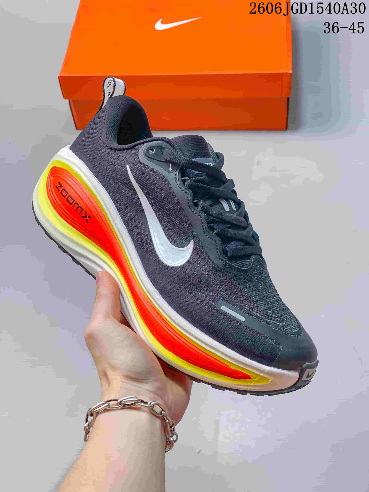 Dark charcoal Nike Vomero Plus running shoe with a light Swoosh and vivid orange and yellow sole accents.