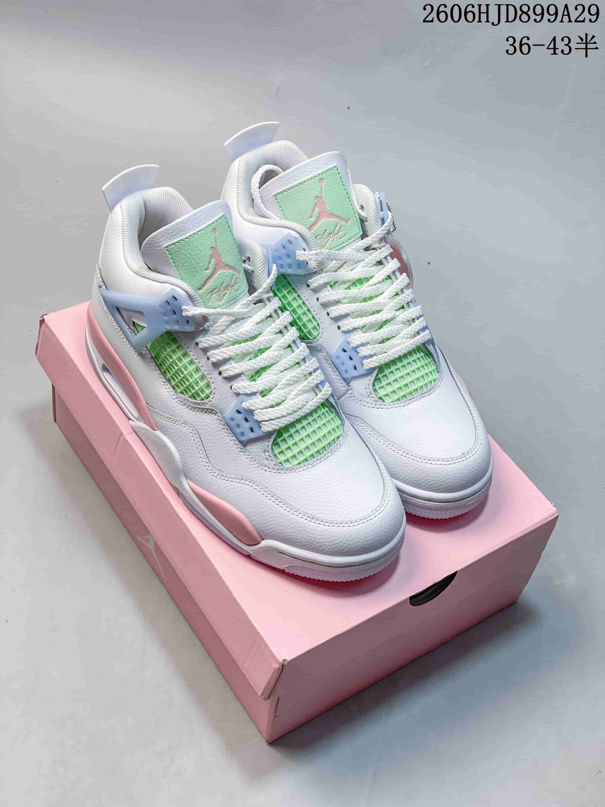 Pair of white Air Jordan 4 Retro sneakers with pink, pale blue, and mint green accents, shown on a pink box