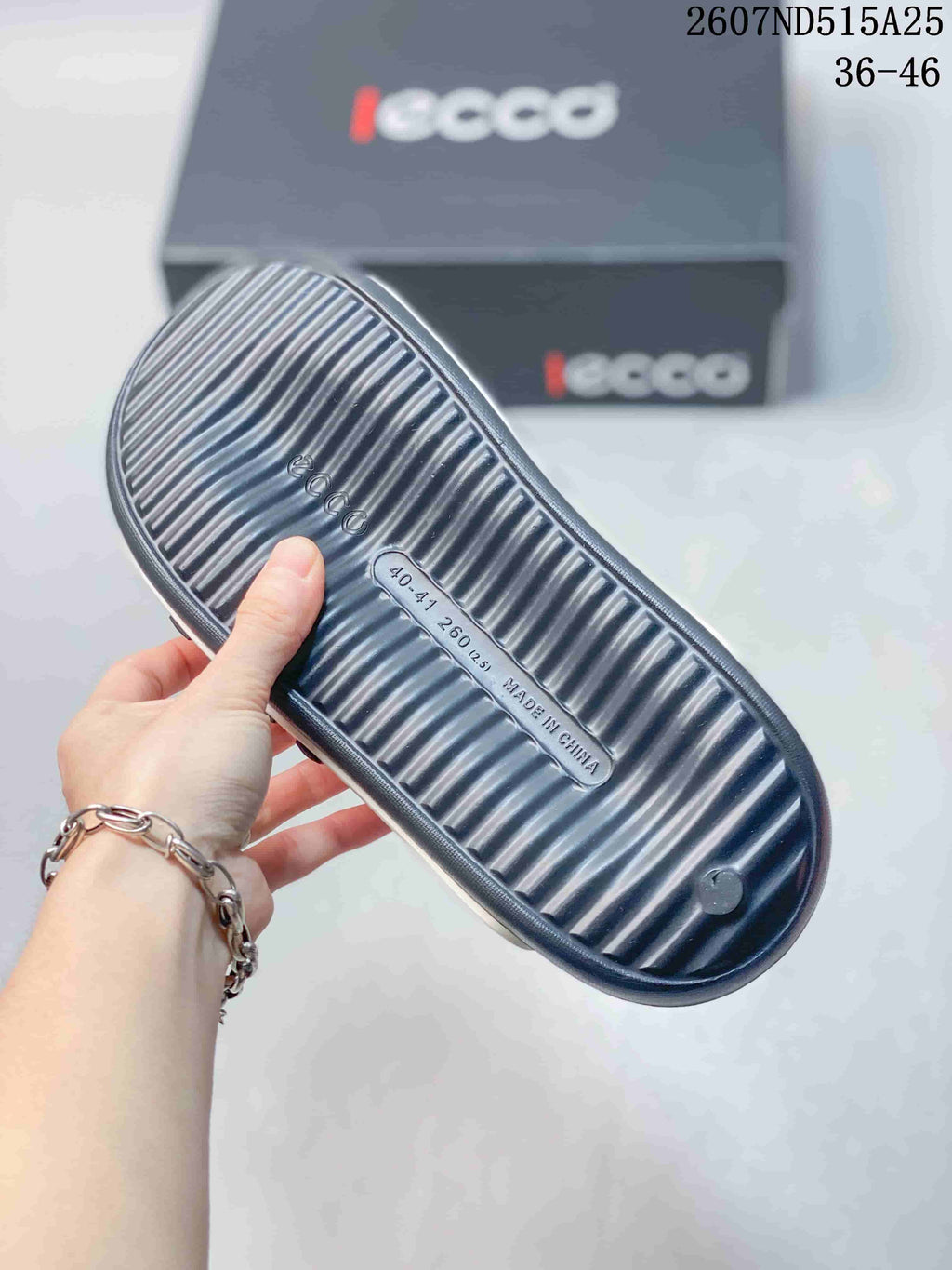 Underside of a navy slide sandal showing a ribbed outsole and molded size marking; branded boxes appear in the background.