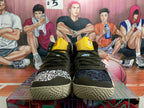 Front view showing yellow tongues, dark laces, contrasting patterned toe panels, and textured soles.