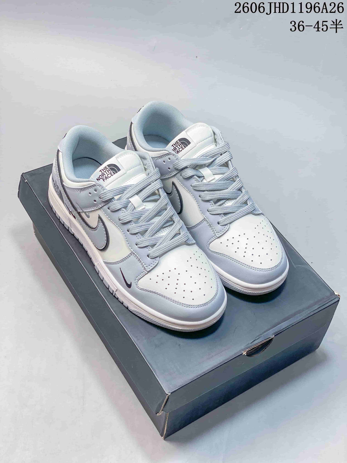 White and pale gray low-top sneakers with dark patterned laces and small swoosh details.