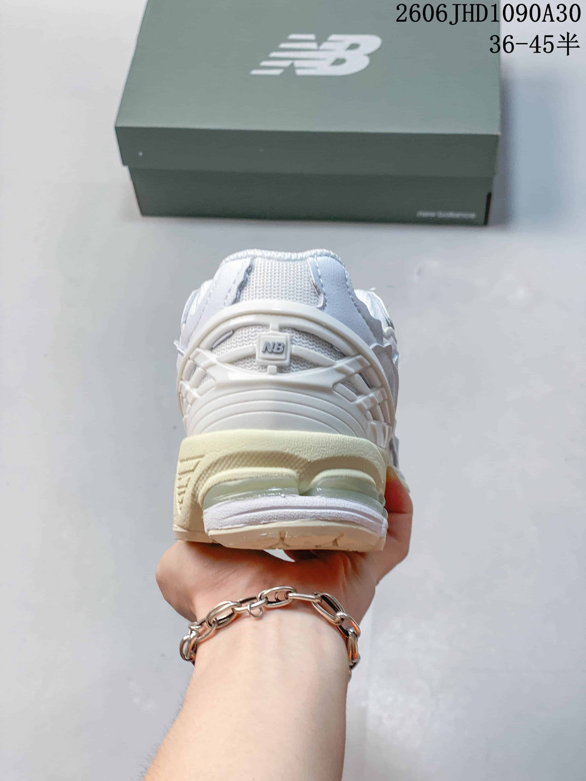 Rear view of a white and silver-toned New Balance M1906R sneaker with a sculpted cream-colored heel.