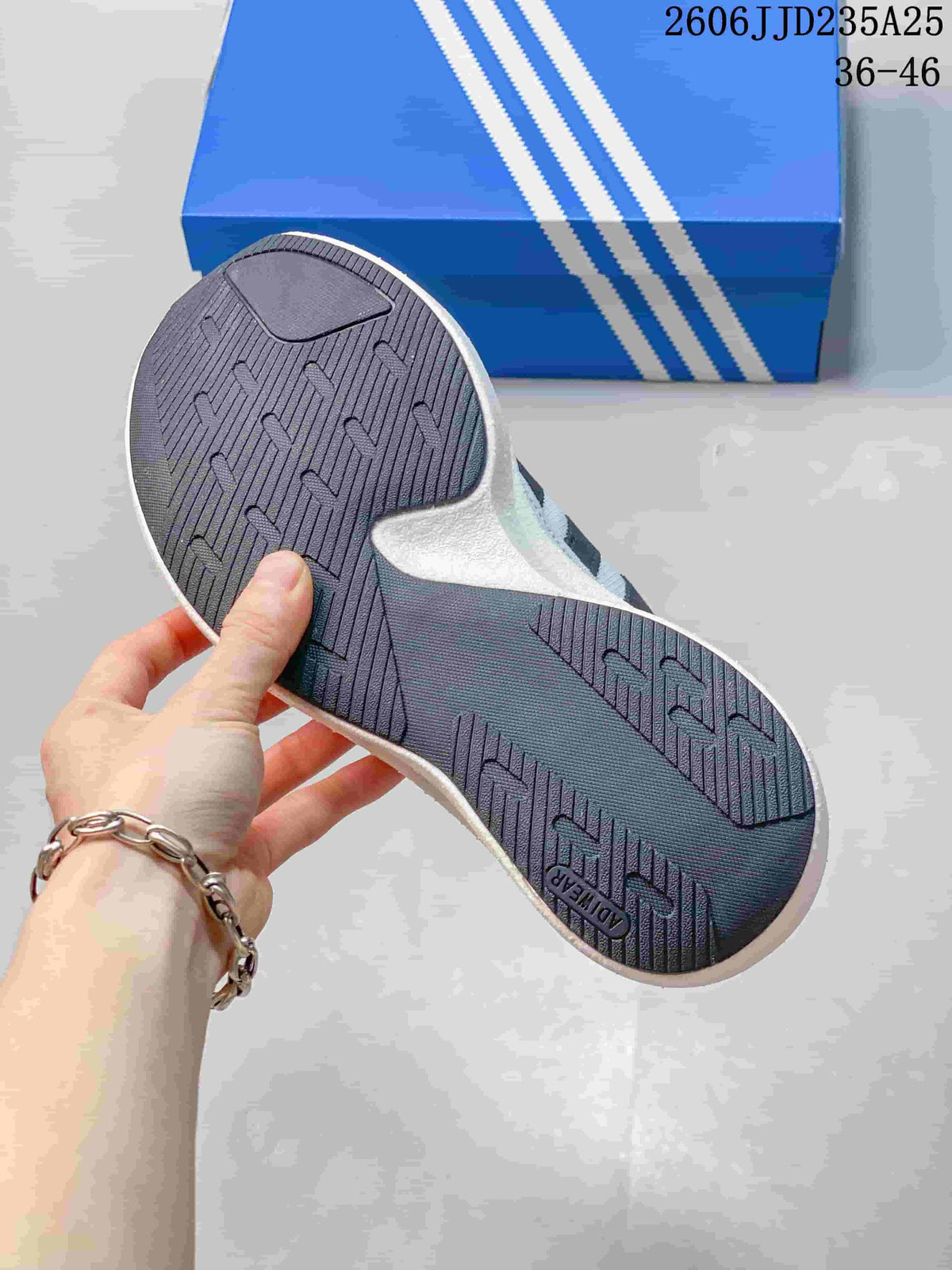 Bottom view showing the textured dark rubber outsole and blue Adidas shoebox.