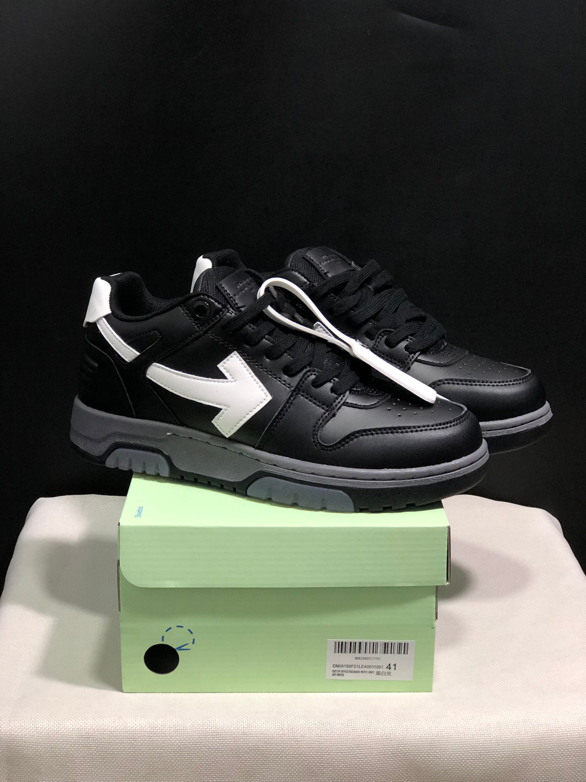Pair of black low-top sneakers with white arrow side details displayed on a light green shoe box; the box label shows size 41.