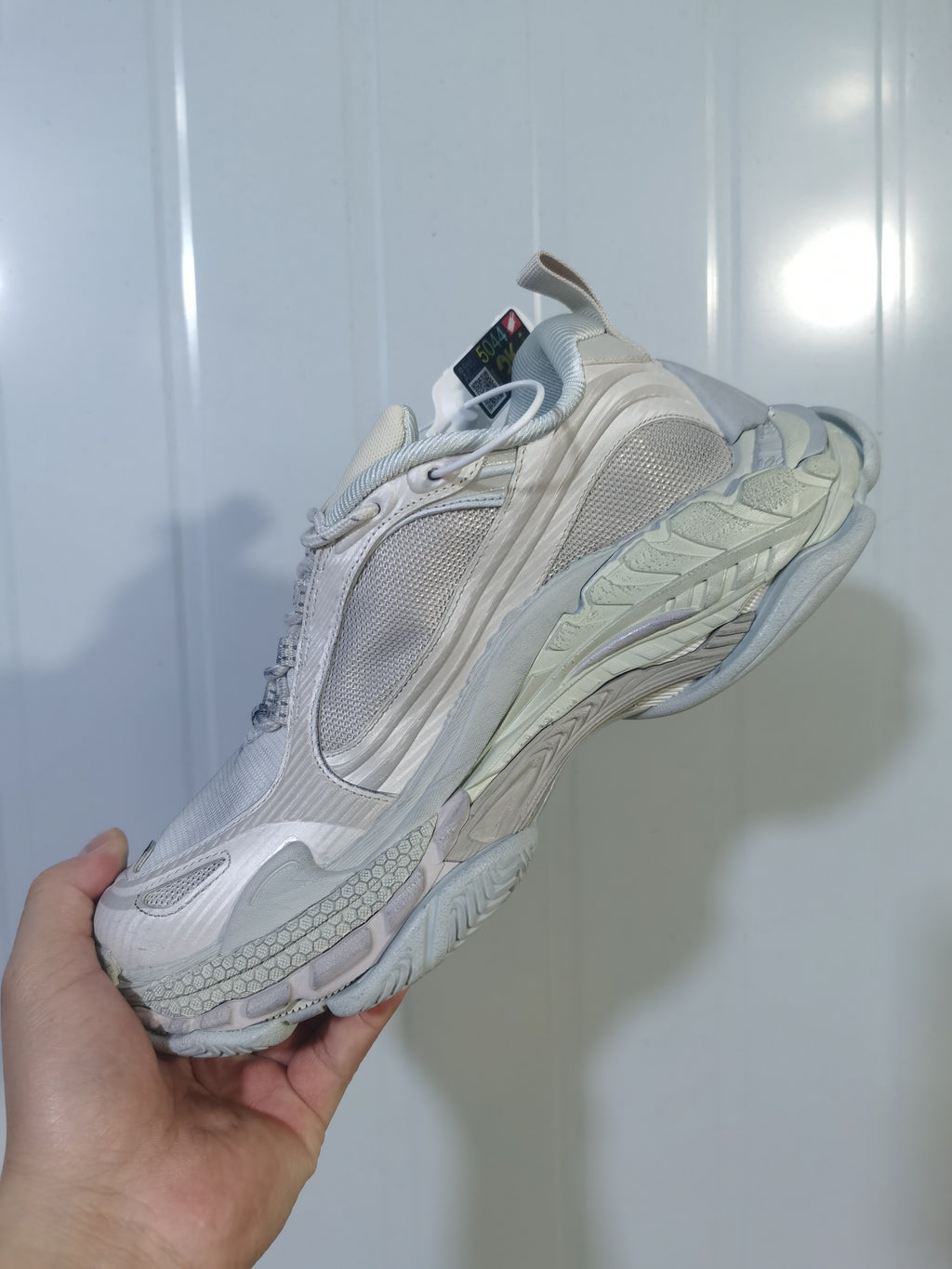 Angled view of an off-white chunky Balenciaga sneaker showing layered panels, mesh sections, and a textured sole.