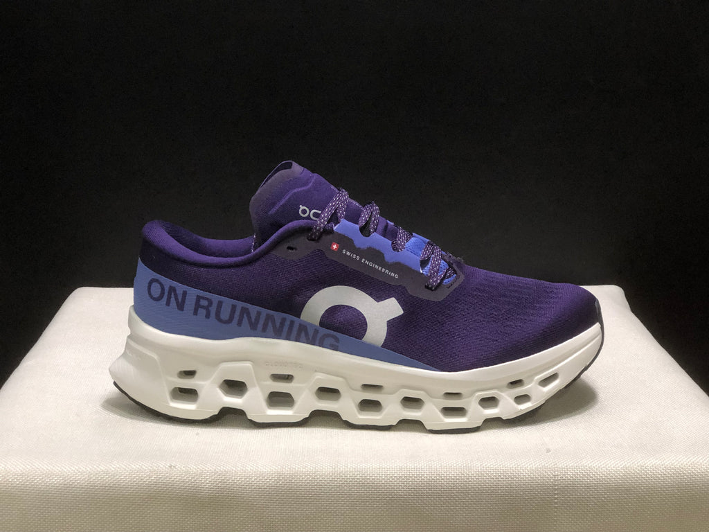 Side profile of a purple On Cloudmonster 3 shoe showing the On logo, lace-up upper, and layered white sole.