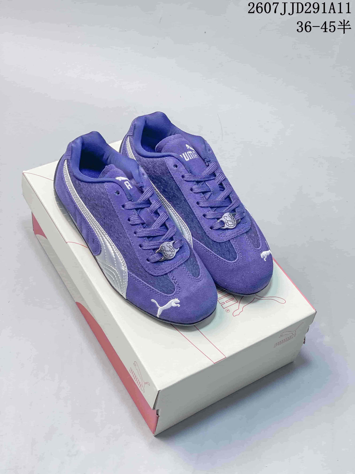 Pair of purple Puma Speedcat sneakers displayed on a Puma shoebox, showing silver side branding and decorative lace charms.