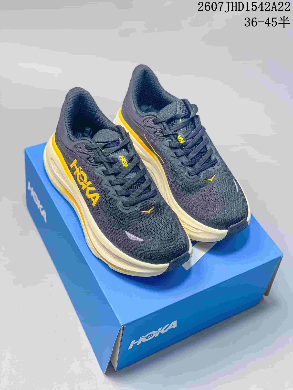 Pair of dark charcoal-black HOKA Bondi 9 sneakers with yellow accents and cream midsoles displayed on a blue shoe box.