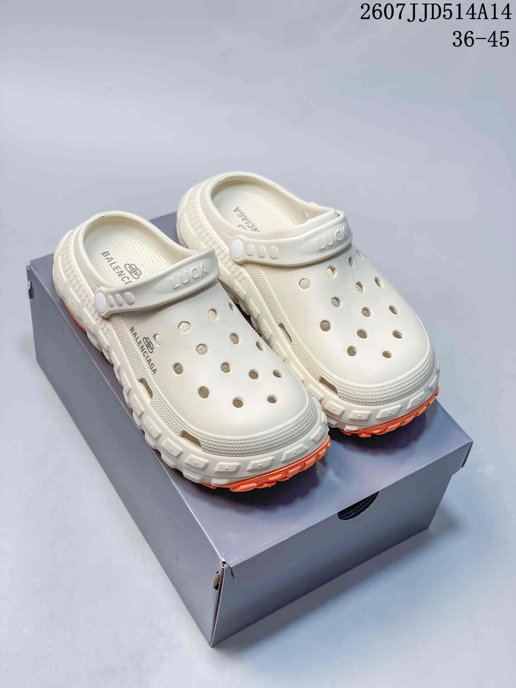 White Balenciaga-branded clogs with perforated uppers, adjustable straps and orange-accented treaded soles displayed on a box.