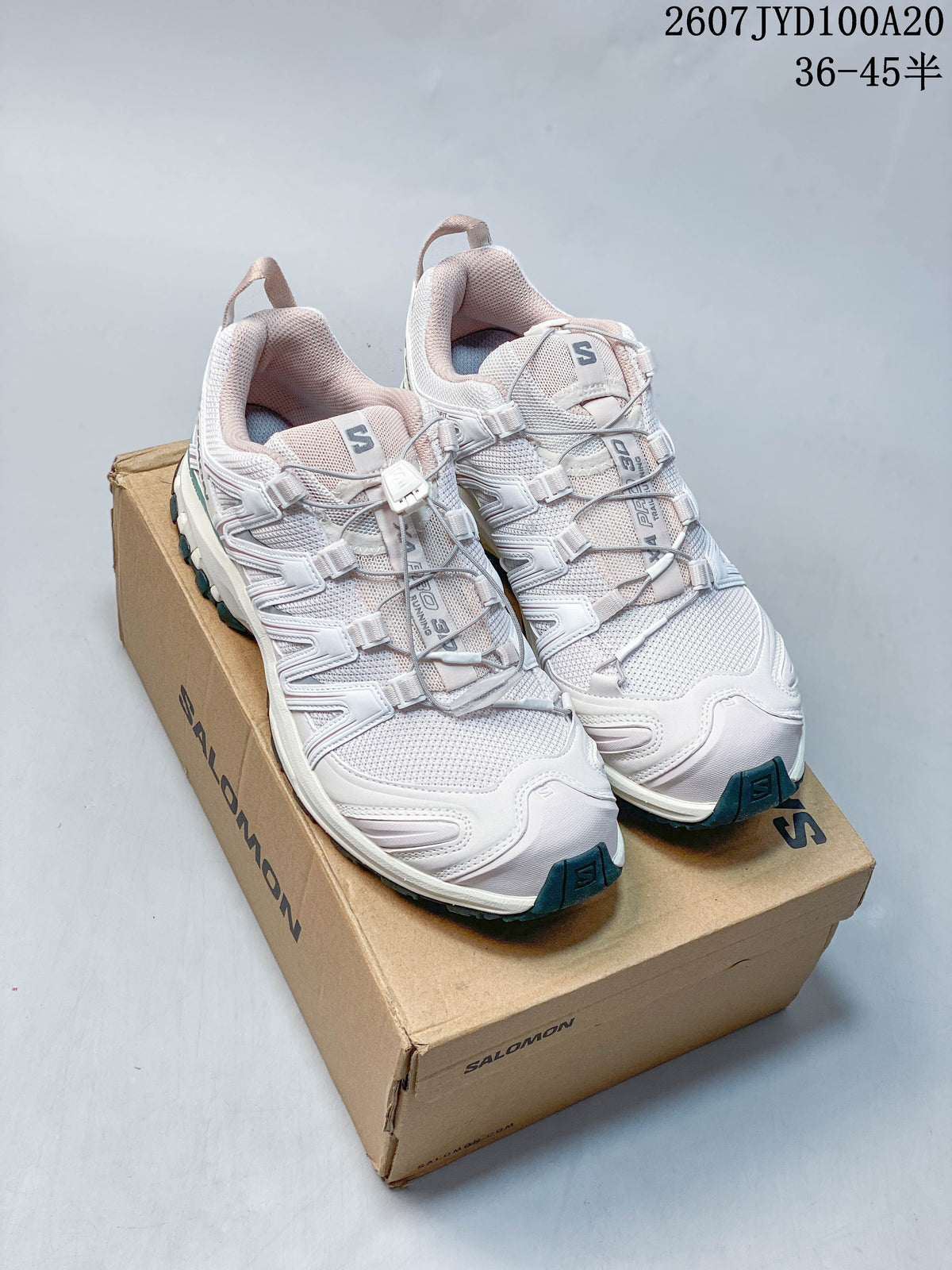 Pair of white Salomon XA PRO 3D sneakers with pink and teal accents displayed on a Salomon shoebox; image text shows style code 2607JYD100A20 and size range 36–45.
